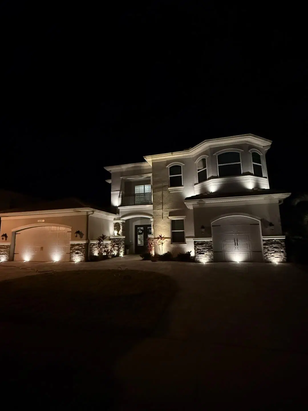 Two-story Odessa home with warm white lighting on entry pillars and facade.