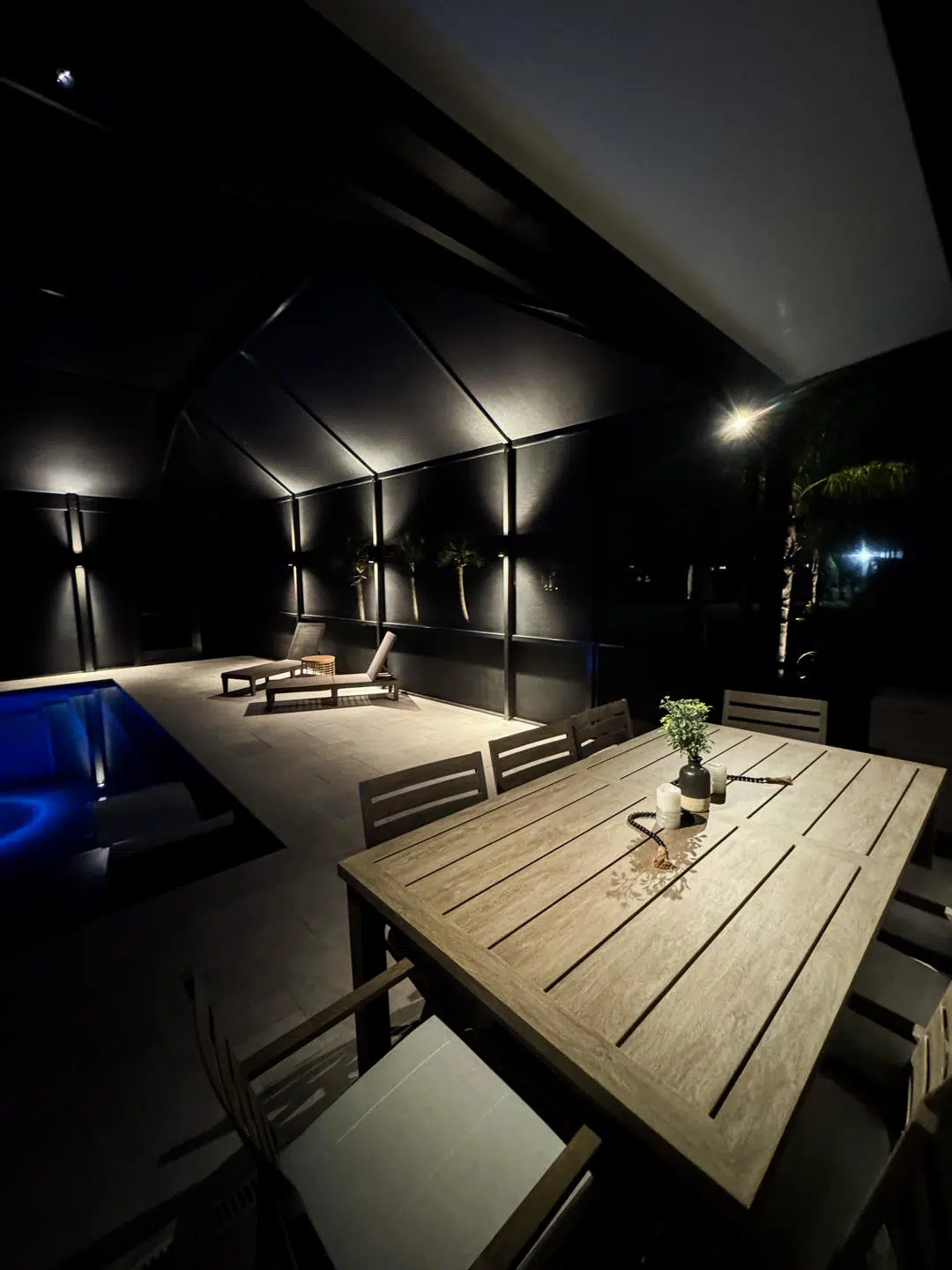 Overhead lighting above an outdoor dining setup under a screened pool enclosure.