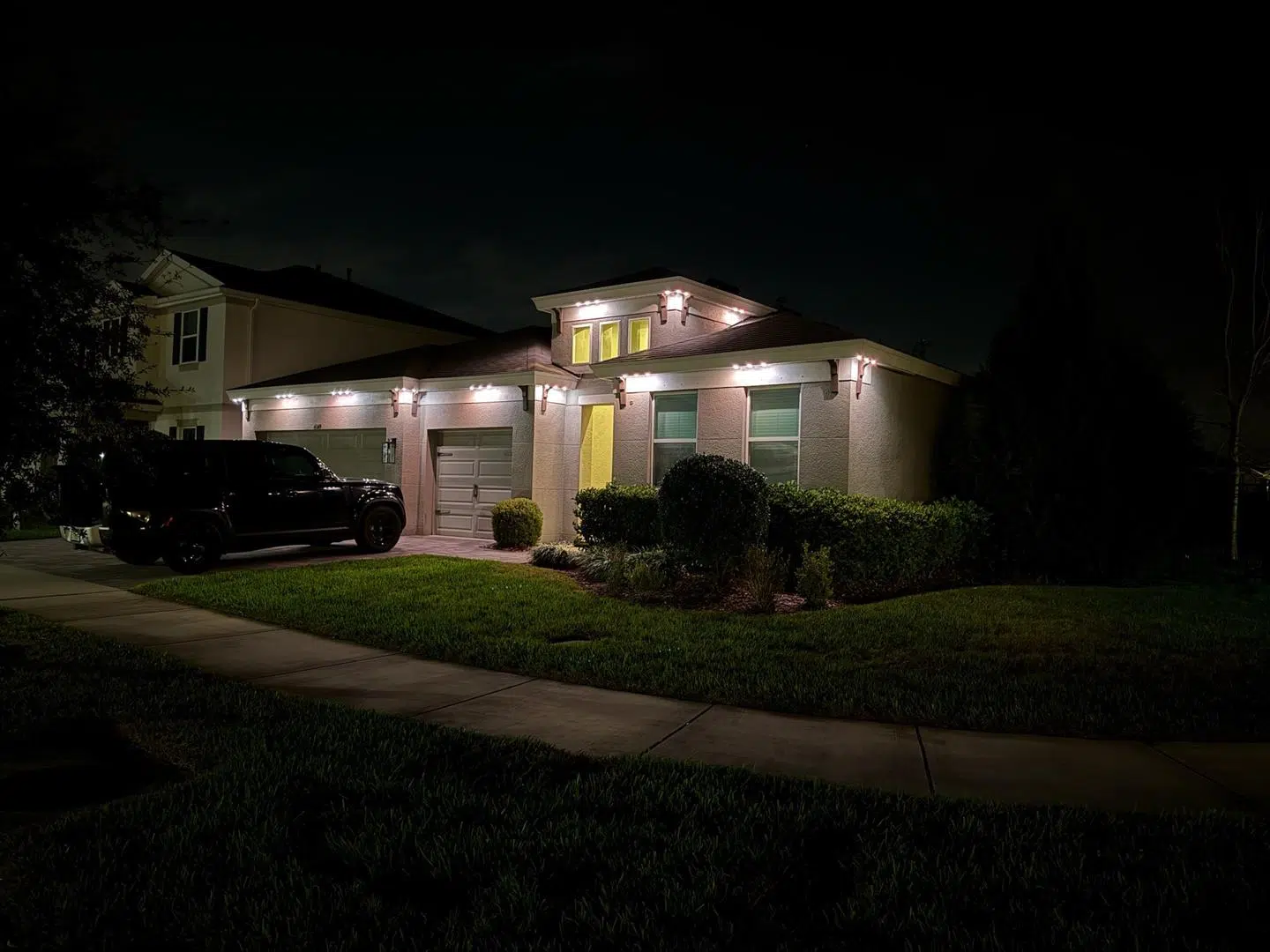 Low-voltage lighting on bushes and roofline of a Trinity single-story home after dark.